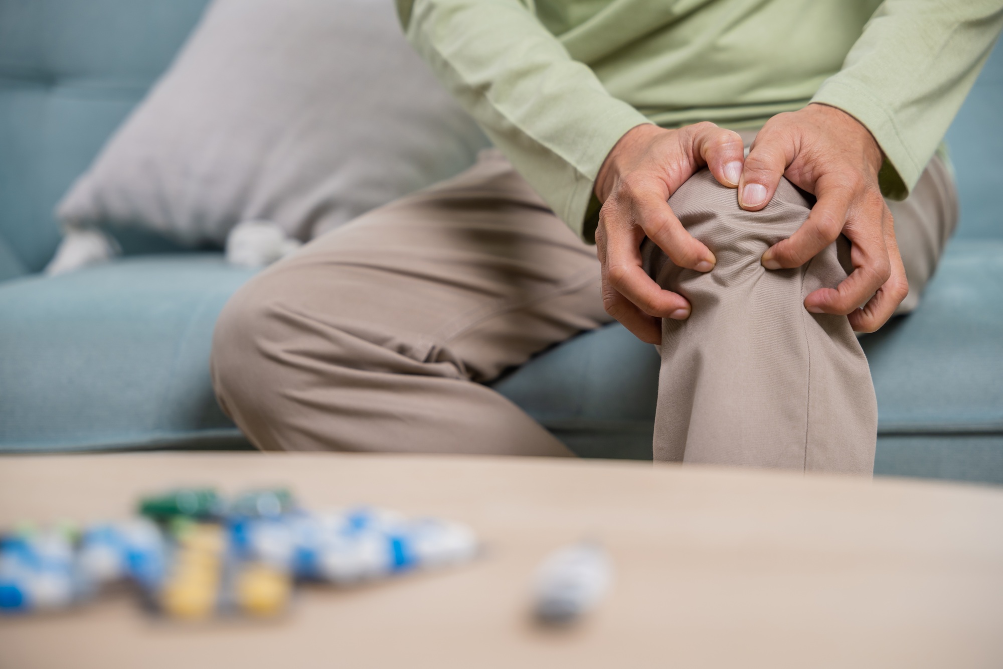 Old man suffering from knee joint pain on sofa living room
